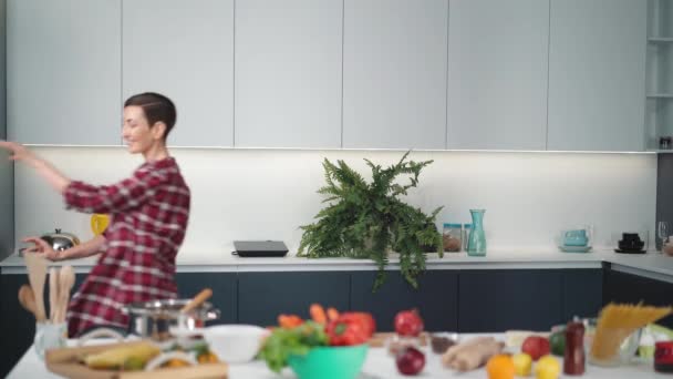 Dançando mulher bonita na cozinha moderna enquanto cozinha o jantar para amigos ou familiares vestindo uma camisa xadrez com um estilo de cabelo bob. Imagens de FHD — Vídeo de Stock