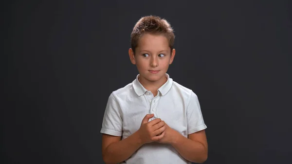 Niño frustrado con camisa blanca tomados de la mano frente a él mientras mira hacia los lados en la esquina superior. Aislado sobre fondo negro — Foto de Stock