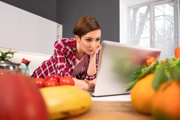 Regarder un film intéressant à l'aide d'un ordinateur portable femme au foyer oublié la cuisine ou la cuisson coincé dans un moniteur. Jeune femme cuisinant dans la cuisine. Vie saine — Photo