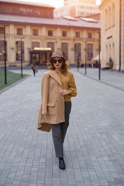 Modèle de mode confiant jeune femme en lunettes de soleil et accroché sur une épaule automne manteau beige marchant dans la rue posant joyeusement pour l'appareil photo. Photo teintée — Photo