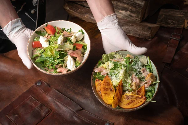 Dos tazones de ensalada de verduras con salmón, queso mozzarella y rebanadas de frutas a la parrilla están sobre una mesa cubierta con un trapo de cuero. Concepto de restaurante. Imagen vertical —  Fotos de Stock