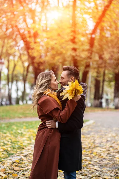 Муж и жена обняли улыбку, глядя друг на друга в осеннем парке. Портрет молодой пары, целующейся наполовину. Фотография влюбленной молодой пары на улице в осеннем парке — стоковое фото