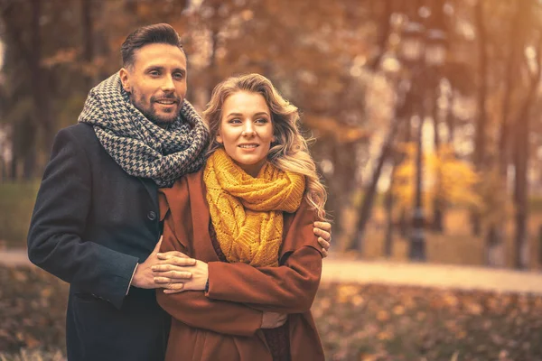 Casal no homem de amor e uma mulher abraçada por trás sorrir olhando para seus filhos no parque de outono. Tiro ao ar livre de um jovem casal apaixonado ter grande momento. Imagem tonificada de outono — Fotografia de Stock