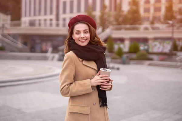 Jeune femme parisienne tenant une tasse réutilisable avec du café debout à l'extérieur. Portrait d'une jeune femme élégante portant un manteau d'automne et un béret rouge à l'extérieur. Accessoires d'automne — Photo