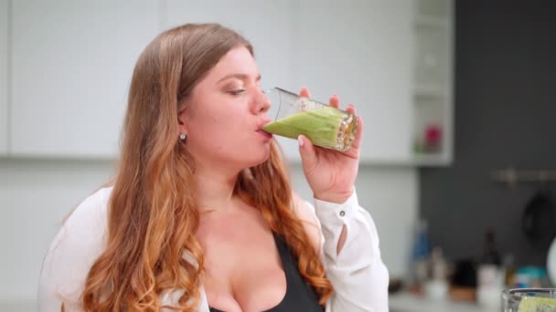 Pití čerstvé okurky nebo avokádové smoothie mladá žena s křivým tělem a dlouhé blond vlasy v moderní kuchyni. Koncept stravy a výživy. FHD — Stock video