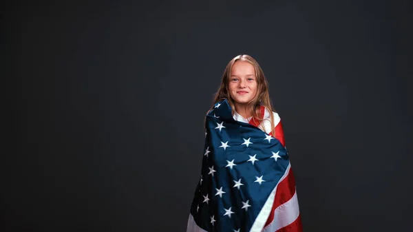 Gadis patriot kecil yang dibalut bendera Amerika Serikat merayakan hari kemerdekaan mengekspresikan patriotisme yang terisolasi dengan latar belakang hitam — Stok Foto