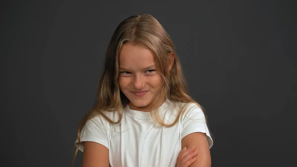 Fecha. Menina de 8,10 anos com as mãos dobradas olha questionavelmente para a câmera vestindo camiseta branca isolada em fundo cinza escuro ou preto — Fotografia de Stock