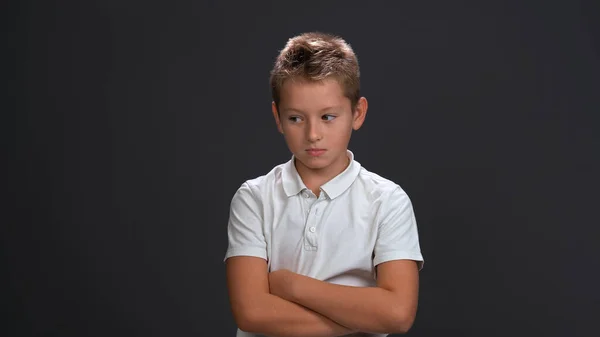 Unzufriedener oder trauriger kleiner Junge, der mit weißem Poloshirt und schwarzer Hose isoliert auf schwarzem Hintergrund die Stirn runzelt — Stockfoto