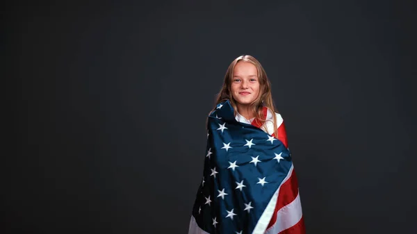 Little girl patriot wrapped in a USA flag celebrates independence day expresses patriotism isolated on black background Royalty Free Stock Images
