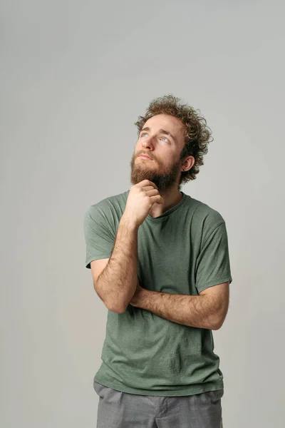 Looking up handsome young man with curly hair in olive t-shirt looking at camera isolated on white background. Portrait of smiling young man with hands folded — Stock Photo, Image