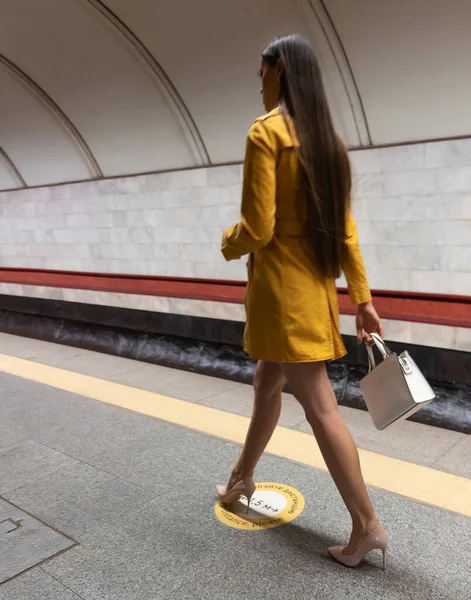 Bakifrån av en promenad på tunnelbanan plattform vacker ung flicka med långa vackra ben bär en gul vårrock och en vit handväska eller handväska i handen — Stockfoto