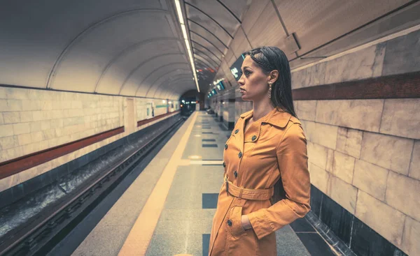 아름다운 소녀가 지하철 승강장에서 서, 멋진 노란색의 스프링 코트를 입고 손에는 흰색 핸드백을 들고 손에는 주머니에는 한 손을 들고 열차를 기다리고 있다 — 스톡 사진