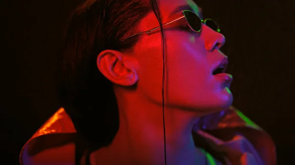 Renkli ışıklarda ceketi ve güneş gözlüğü takan kızın şehvetli portresi. Siyah arka planda neon ışıklı güzel bir kız. Gece kulübü, Parti — Stok fotoğraf