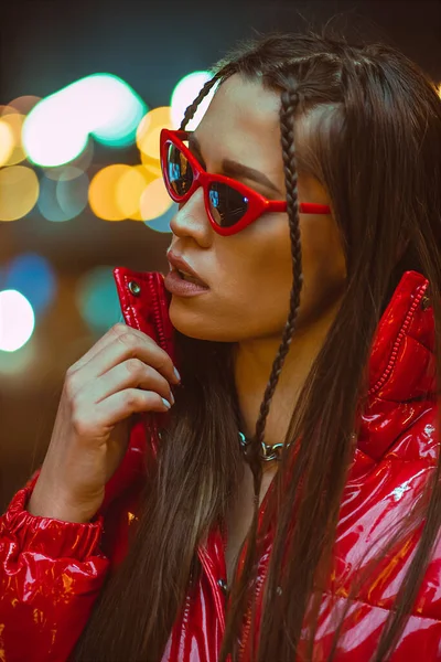 Gadis muda dengan kacamata potret mode luar ruangan dengan rambut dikepang memakai jaket merah ke bawah dan mode pada lampu neon jalan. Klub malam fashion. Gadis dan lampu neon — Stok Foto