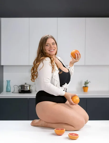 Здоровое питание счастливое фигурное тело молодой женщины с длинными светлыми волосами жонглируя фруктами сидя на современном кухонном столе, смешивая свежие фрукты для здорового смузи. Диета и питание — стоковое фото