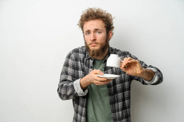 Good looking man with curly hair and beard holding inverted cup showing No coffee, guy wearing plaid long sleeve shirt isolated on white background. Crisis and lockdown concept — Stock Photo, Image