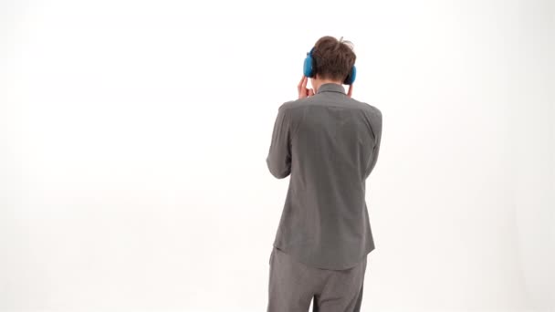 Danse écouter de la musique debout à la caméra beau jeune homme en tenue de sport grise portant des écouteurs sans fil bleus. Drôle de jeune homme dansant écouter sa chanson préférée. Images 4K — Video
