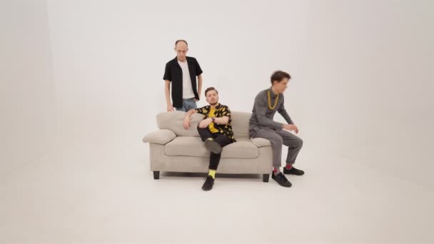Helyet cserél három fiatal jóképű férfi mozog a kanapén elfoglalva a főhelyet, és elviszi a jelenet kanapé elszigetelt fehér háttérrel. 4K felvétel — Stock videók