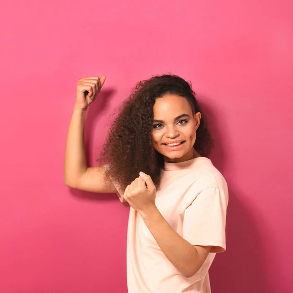 Šťastná krásná mladá Afroameričanka dívající se pozitivně na kameru s broskvovým tričkem ukazujícím svaly izolované na růžovém pozadí. Krásný koncept. Čtvercové ořezy — Stock fotografie