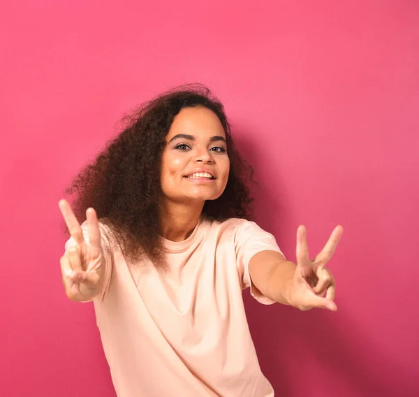 Ευτυχής αποστολή χειρονομία ειρήνευσης με τα δύο χέρια όμορφη νεαρή Αφροαμερικανή γυναίκα κοιτάζοντας θετικά στην κάμερα φορώντας όμορφα t-shirt απομονώνονται σε ροζ φόντο. Έννοια ομορφιάς. Τετραγωνική καλλιέργεια — Φωτογραφία Αρχείου