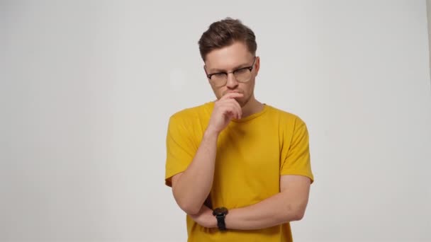 Портрет красивого молодого человека в очках, выглядящего разочарованным или напряженным, нервно кусающего палец, размышляющего над идеей, изолированной на белом фоне. 4K видео — стоковое видео