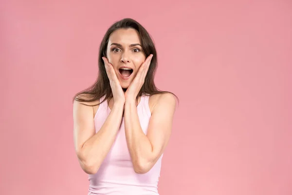 OMG surpreendeu muito jovem mulher vestindo camiseta rosa com as mãos no rosto, animado e expressão de alegria em seu rosto com emoções positivas. Expressões faciais, emoções, sentimentos — Fotografia de Stock