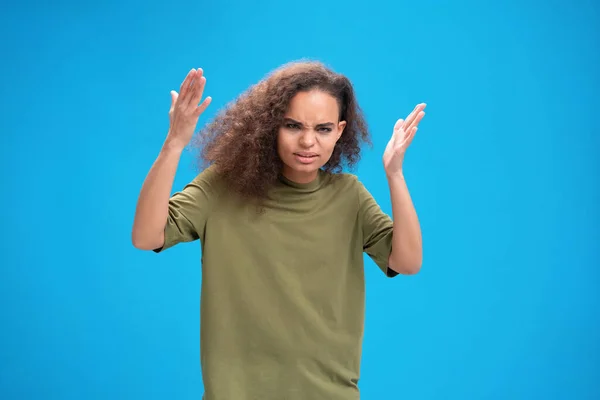 A dühös afro-amerikai lány felemelte a kezét, és csalódottan nézett a kamerába, kék alapon elszigetelt olíva pólóban. Emberi érzelmek, arckifejezés fogalma — Stock Fotó