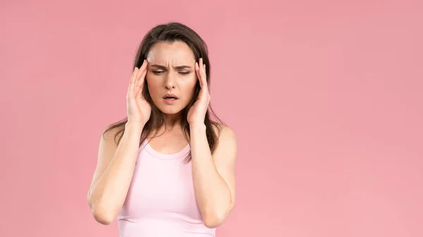 Tiene migraña o dolor de cabeza severo mientras masajea el lóbulo temporal de la cabeza, una mujer joven que usa una camiseta rosa con las manos en la cabeza. Emociones humanas, concepto de expresión facial —  Fotos de Stock