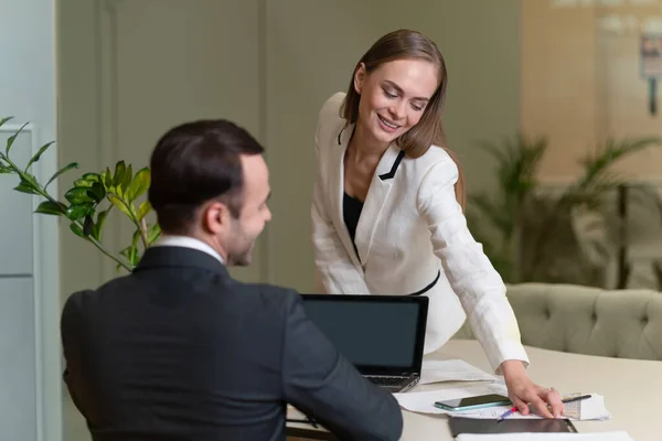 Dos colegas jóvenes y atractivos coqueteando en la oficina. Mujer joven sentada en la mesa y sexualmente inclinada hacia un hombre joven. Coqueteando en el lugar de trabajo. Oficina romance — Foto de Stock