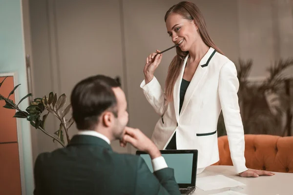 Młoda kobieta siedząca na stole i seksualnie patrząca na młodego mężczyznę. Dwóch młodych i atrakcyjnych kolegów flirtuje w biurze. Flirtowanie w miejscu pracy. biurowy romans — Zdjęcie stockowe