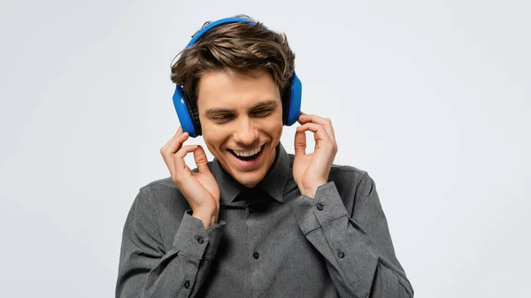 Χαρούμενος τύπος με γκρι πουκάμισο που ακούει μουσική φορώντας μπλε ασύρματα ακουστικά απολαμβάνοντας ήχο με κλειστά μάτια. Ευτυχισμένος νεαρός ακούει το αγαπημένο του τραγούδι ή τραγούδι — Φωτογραφία Αρχείου