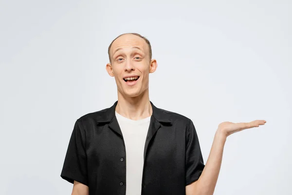 Holding a banner on a left hand free place for your text young bald man in black shirt with white t-shirt under. Happy young man showing copy space for your product isolated on white background — Stock Photo, Image