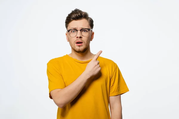 Señalando hacia arriba a un espacio de copia gratis guapo joven en gafas de ojo sorprendido con la expresión sorpresa en su cara mirando a la cámara. Retrato de hombre casual joven aislado sobre fondo blanco —  Fotos de Stock