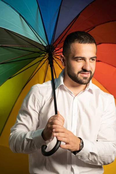 Supporting minorities straight handsome guy with a rainbow umbrella behind his back. Healthy fashion lifestyle, people sincere emotions, cold season concept. Handsome guy in support of LGBTQ society — Stockfoto