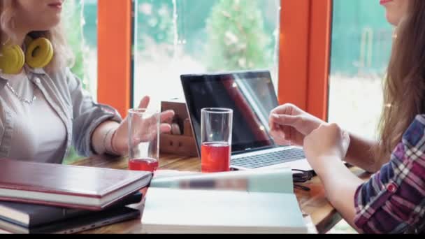 Fermez deux étudiantes de première année qui parlent étudient dans un café en partageant leurs histoires avec des lumières en arrière-plan avec des livres ouverts et un ordinateur portable sur la table. Images 4K — Video