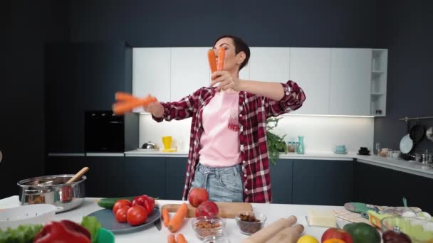 Wirft gewaschene Möhren beim Jonglieren hoch und erwischt keine charmante kurzhaarige Hausfrau, die in der Küche Möhrenkuchen zubereitet. Gesunde Ernährung zu Hause. Konzept für gesunde Ernährung — Stockvideo