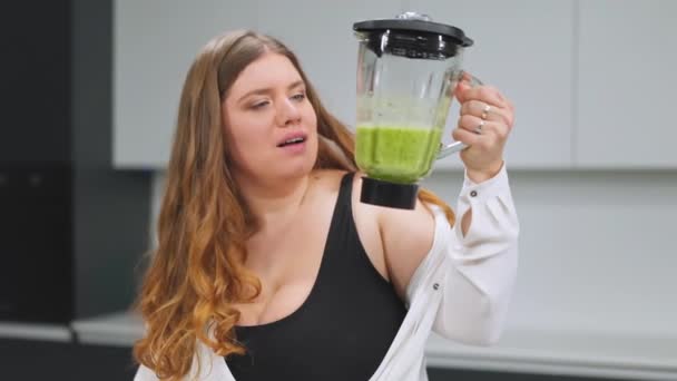 Ung kvinna som gör omad hälsosam detox juice gjord med mixern hemma. Göra vegan keto ung kvinna med kurvig kropp stående på modernt kök. Diet och näringskoncept. FHD — Stockvideo