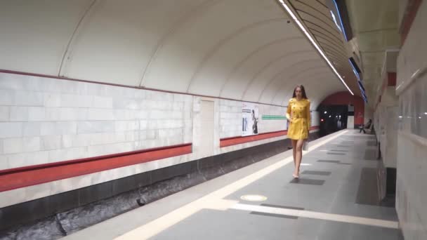 羽の上を歩くことは、黄色の春のコートと彼女の手の中に白いハンドバッグの長い足を持つ美しい若い女の子です。FHD。キエフ・メトロ、キエフ、ウクライナ。2020年12月 — ストック動画