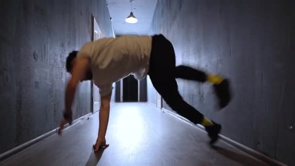 Νεαρός χορευτής χιπ χοπ κάνει τον χορό του μπροστά στην κάμερα. Χορεύοντας σε μια αχτίδα φωτός σε ένα μακρύ στενό σκοτεινό διάδρομο με πολλές λευκές πόρτες και στις δύο πλευρές. Βίντεο 4K — Αρχείο Βίντεο
