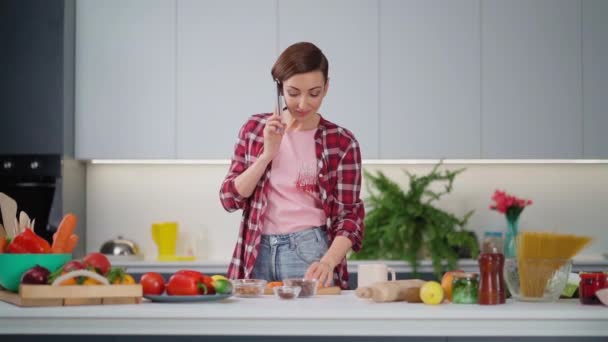 Talking on the phone eating carrots pretty woman with a short hairstyle prepares food in the kitchen. Healthy food at home. Healthy food leaving - vegan concept. New house concept. Slow motion Royalty Free Stock Video