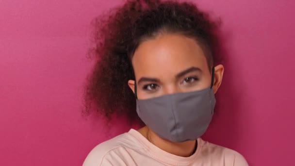 Zgadzam się, kiwnięcie głową nosząc maskę wielokrotnego użytku Afroamerykańska urocza dziewczyna w eleganckim t-shirt, aby zapobiec od korony COVID-19 i zakażenia SARS cov 2 izolowane na różowym tle — Wideo stockowe
