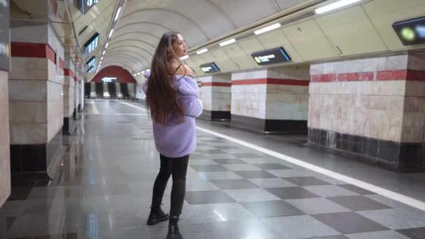 Modelo menina bonita no metro vestindo elegante casaco de pele sintética roxo andando em câmera lenta. Feminino com maquiagem de luxo, cabelo longo em roupa elegante — Vídeo de Stock