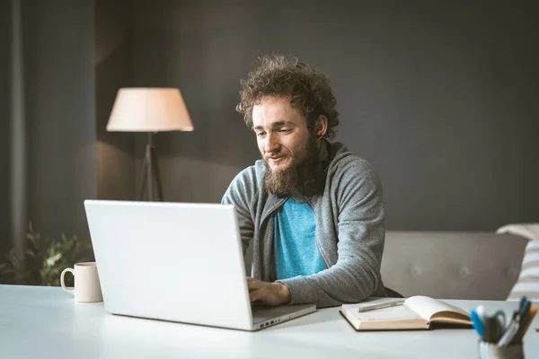 The copywriter works from home to write the article. A young man with curly hair is typing on a laptop. Work at home is a concept.