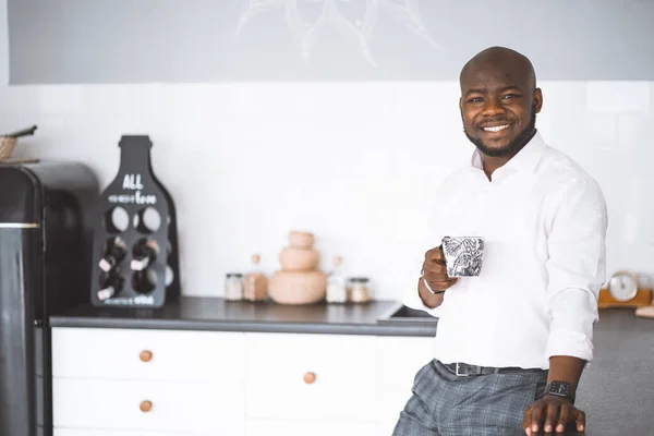Επιτυχημένος νεαρός επιχειρηματίας. Αφρο-Αμερικανός που χαμογελάει στην κουζίνα με ένα φλιτζάνι στο χέρι. Πλούσιος επενδυτής στο σπίτι του πριν τη δουλειά. Έννοια της νίκης, προσωπική ανάπτυξη — Φωτογραφία Αρχείου