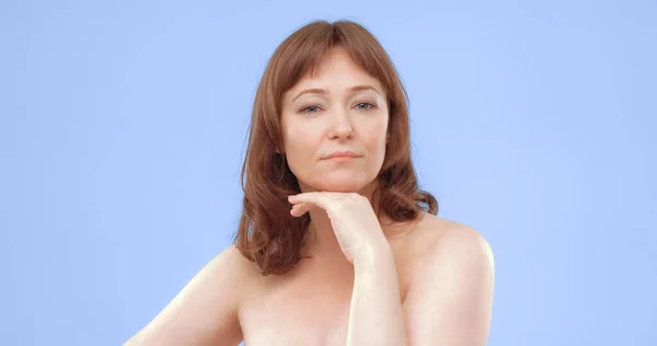 Confident middle aged woman looks at camera with his hand near the chin. Nude beautiful Caucasian woman with well-groomed skin. Body and face care concept — Stock Photo, Image