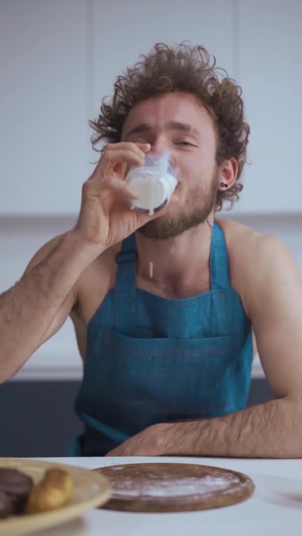 Vídeo vertical. Un vídeo divertido. Chico joven en la cocina con comida y leche. Video de stock