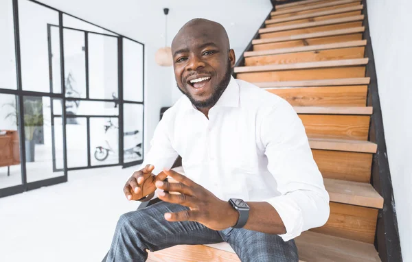 Успешный молодой бизнесмен. Афроамериканец делится своей историей успеха. Молодой человек сидит на лестнице в своем роскошном доме. Концепция победы, личностный рост. Высокое качество и успешная молодежь — стоковое фото