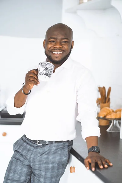 Framgångsrik ung affärsman. African American Man står med bägare i sitt kök. Han är glad och ler. Begreppet lyx, rikt liv — Stockfoto