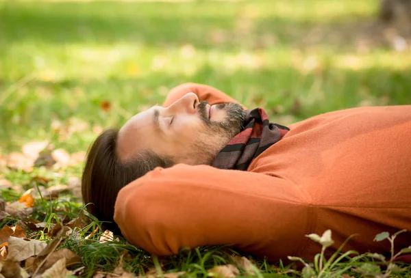 Handsome middle-aged man lying on the autumn leaves in park — Stok fotoğraf