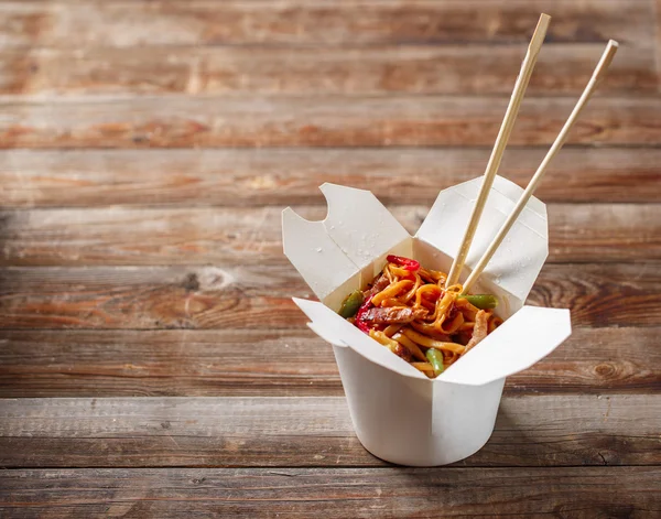 Fideos con cerdo y verduras en caja para llevar sobre mesa de madera —  Fotos de Stock